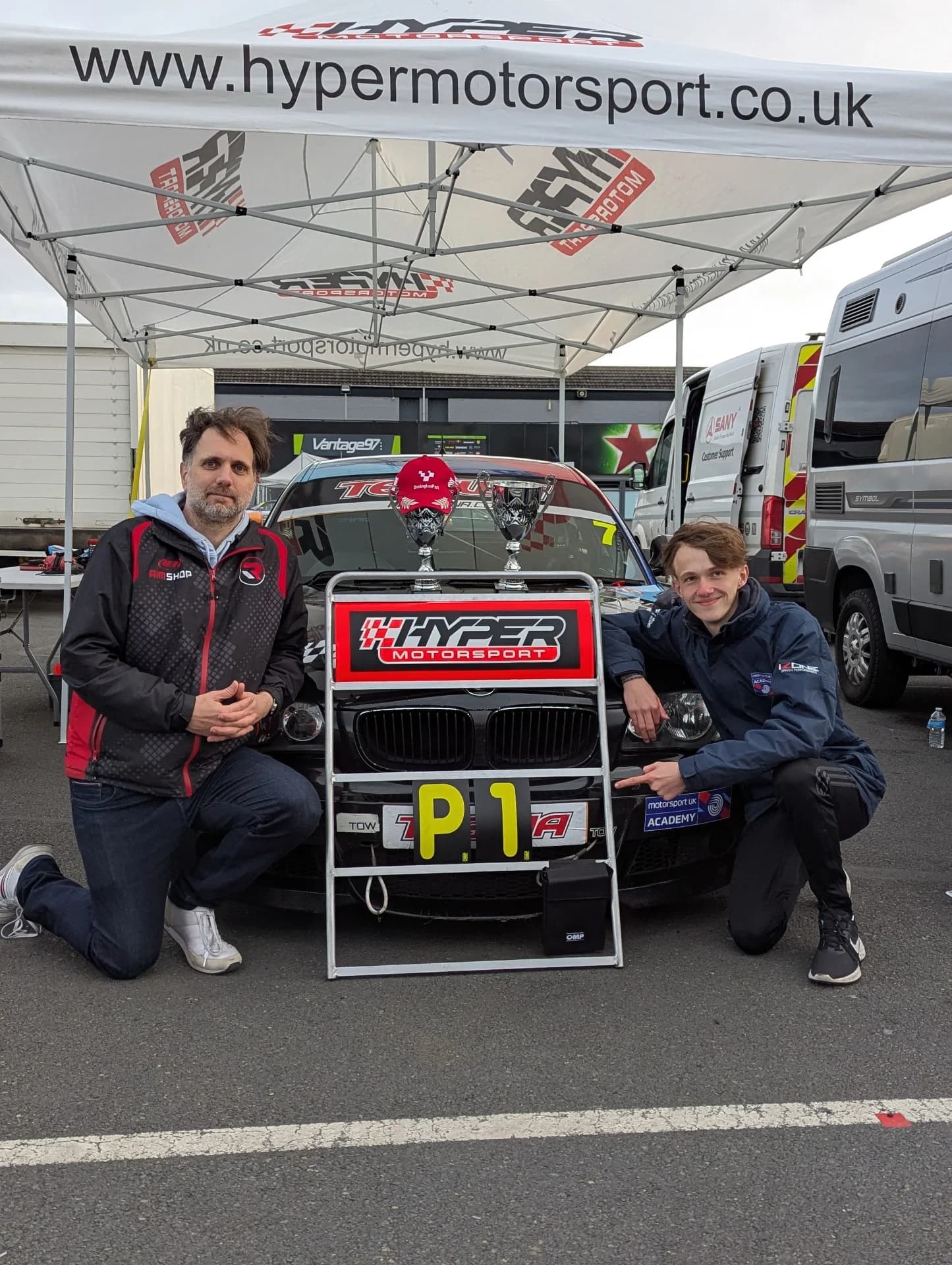 Matthew Swatton & Jez Banks crouche next to the pit board showing P1 after their win at Donington Park GP
